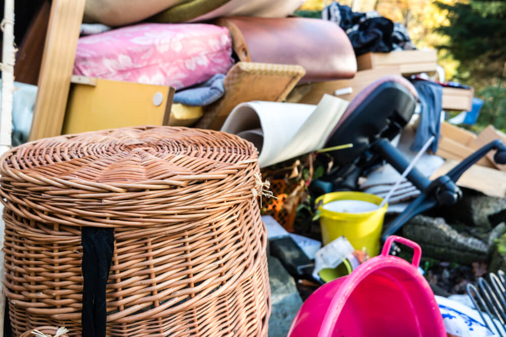 Close-up of a cluttered pile of household items including a wicker basket, pink and yellow buckets, and furniture, creating a chaotic scene.